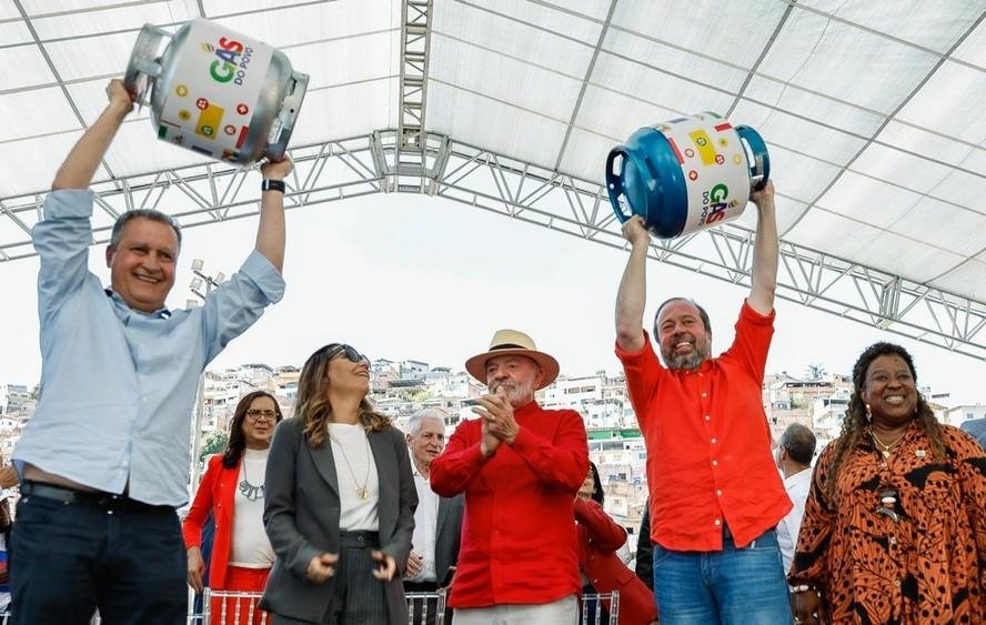 Os ministros Rui Costa e Alexandre Silveira levantam botijões de gás, em evento ao lado de Lula